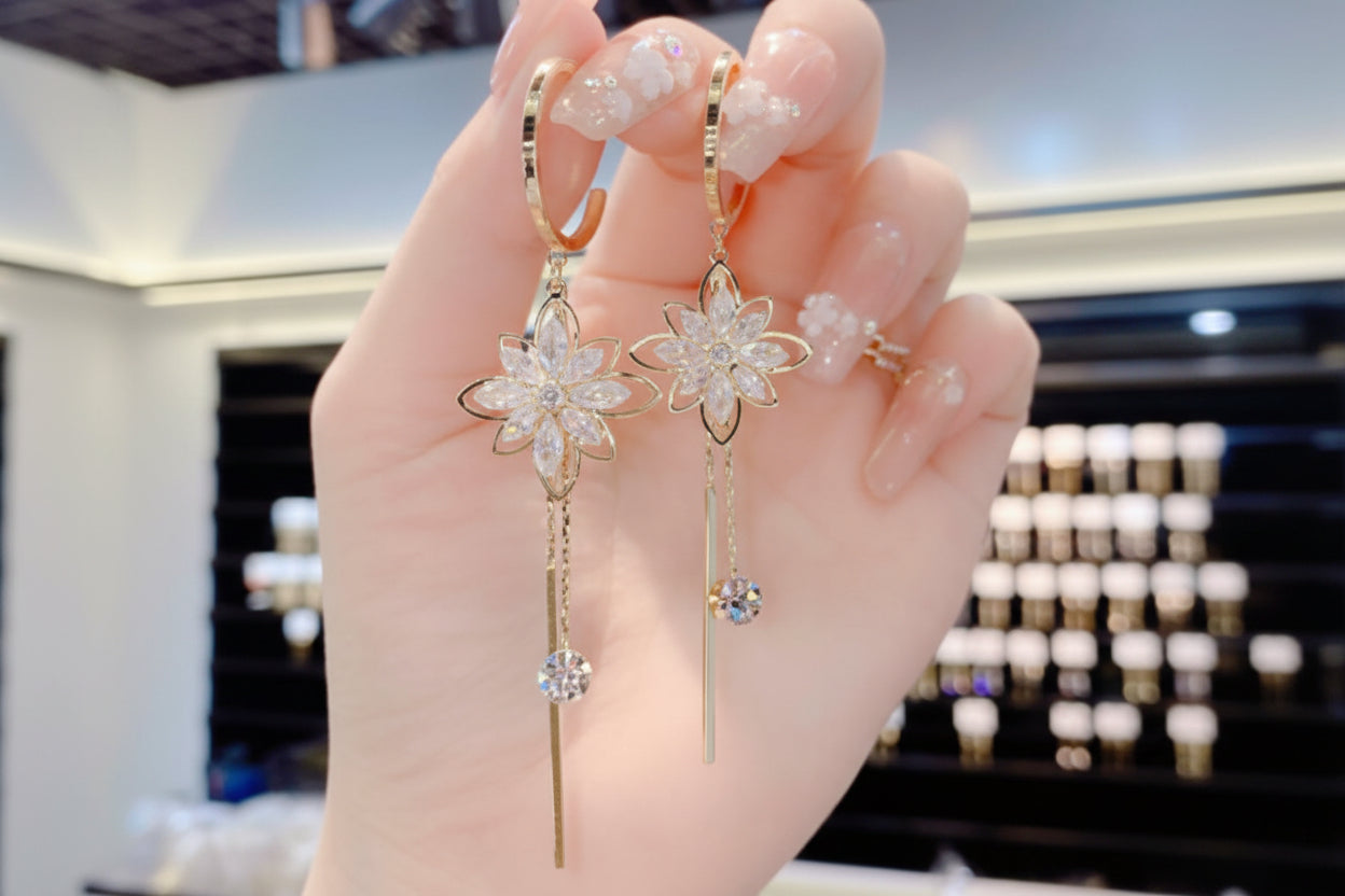 Gold floral earrings with clear stones held by a hand against a blurred background