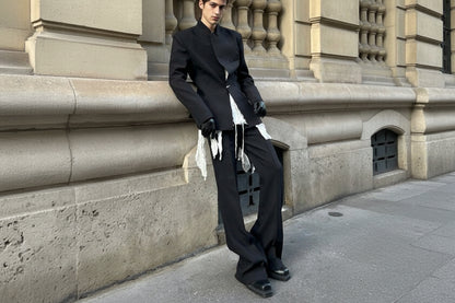 Person wearing a black outfit with white accents against a stone building background