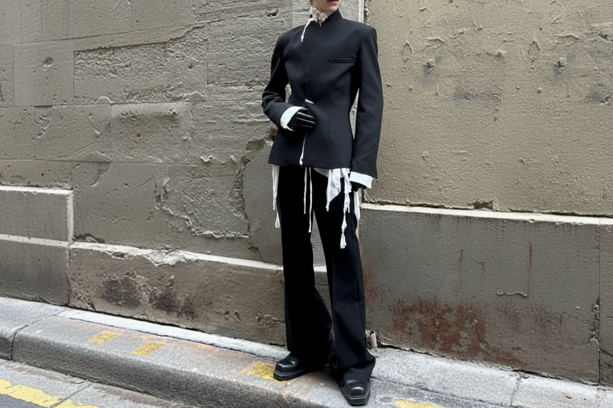 Person wearing a black outfit with white accents against a textured wall.