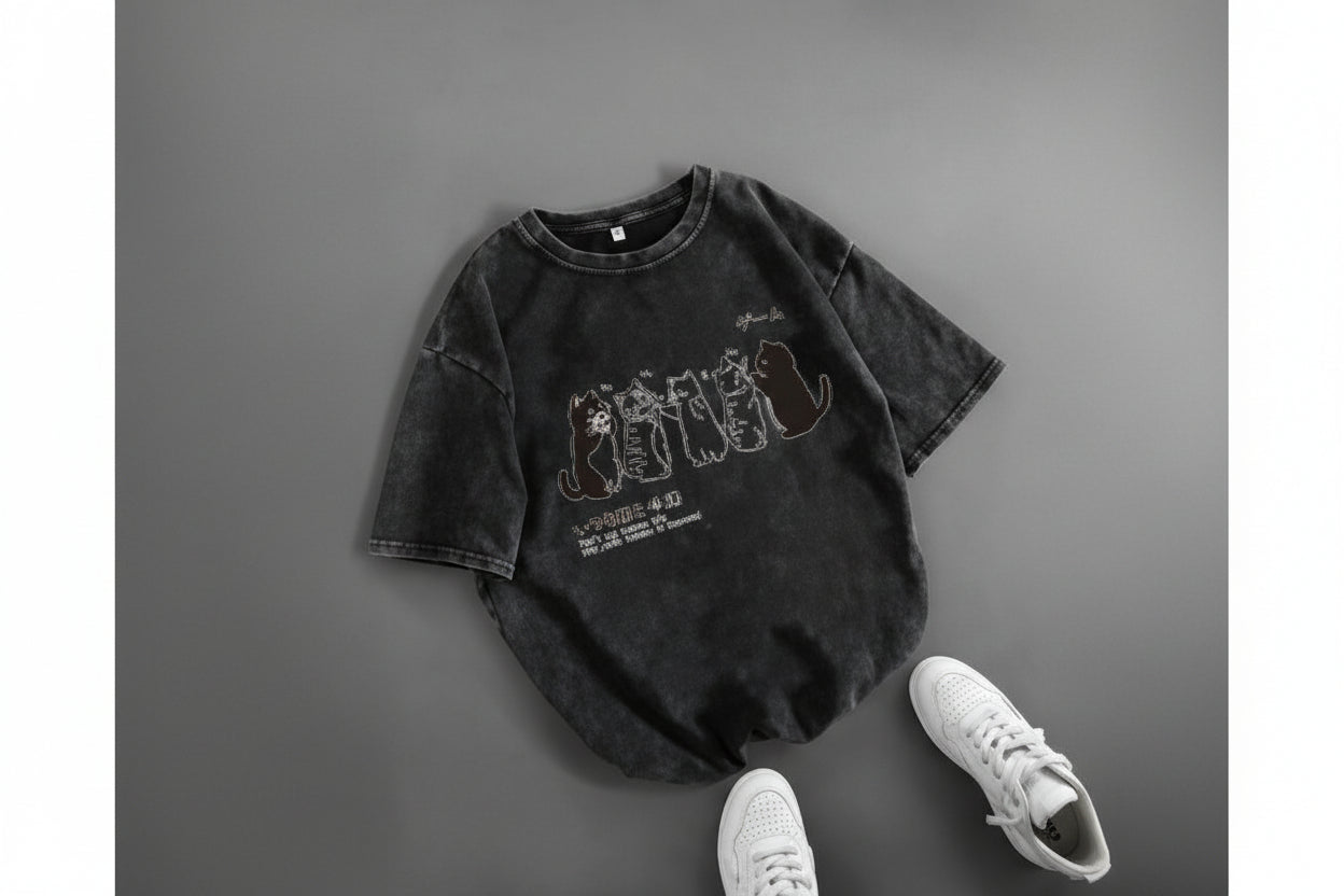 Black t-shirt with graphic design on a gray surface with white sneakers.