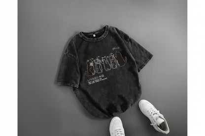 Black t-shirt with graphic design on a gray surface with white sneakers.