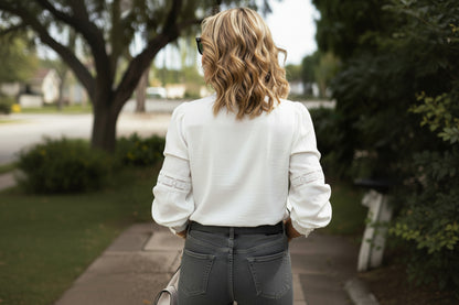 Person wearing a white sweater and gray jeans walking outdoors.