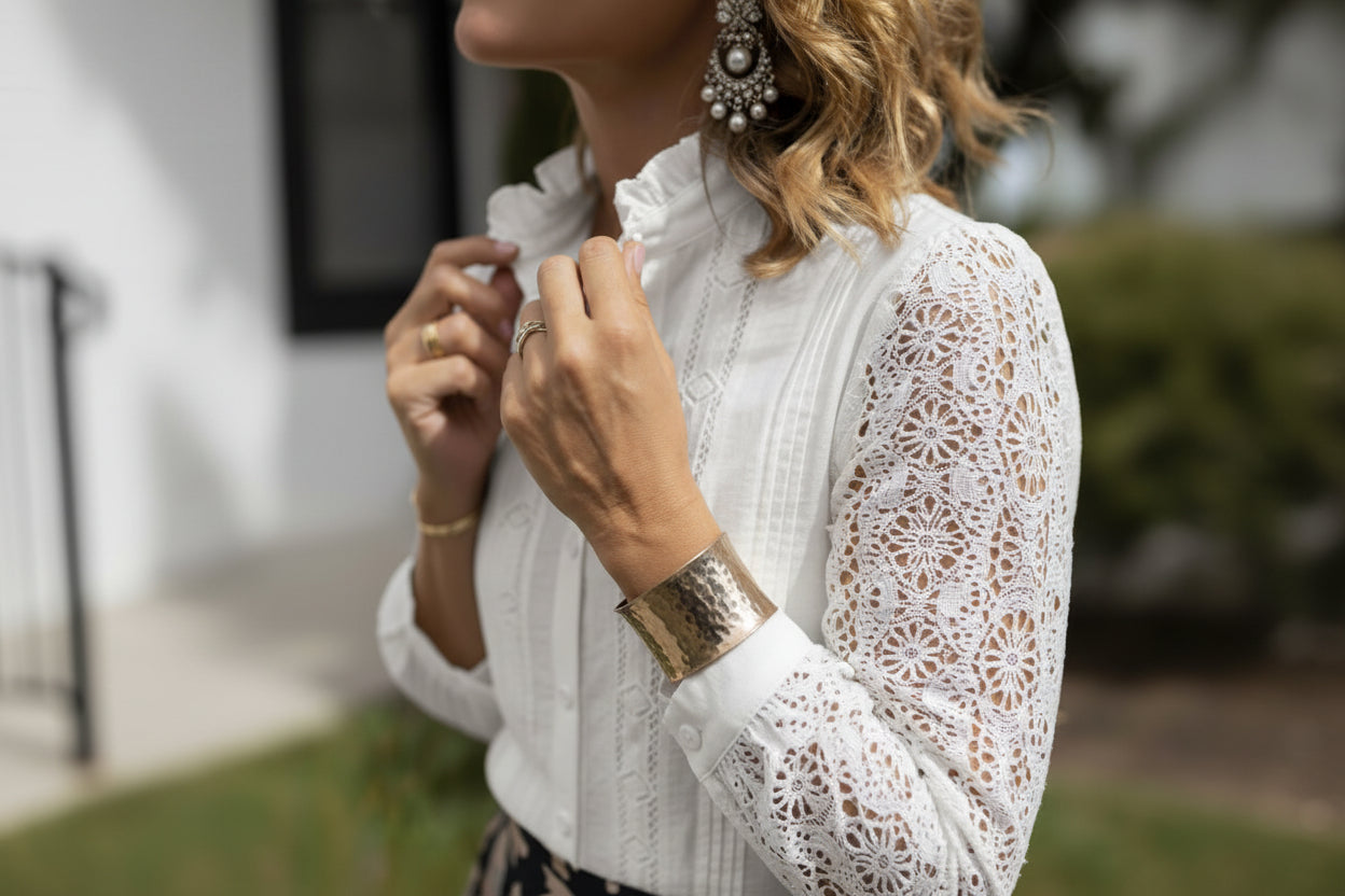 Person wearing a white blouse with jewelry, including a watch and bracelets, with a blurred outdoor background.