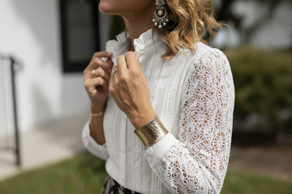 Person wearing a white blouse with jewelry, including a watch and bracelets, with a blurred outdoor background.