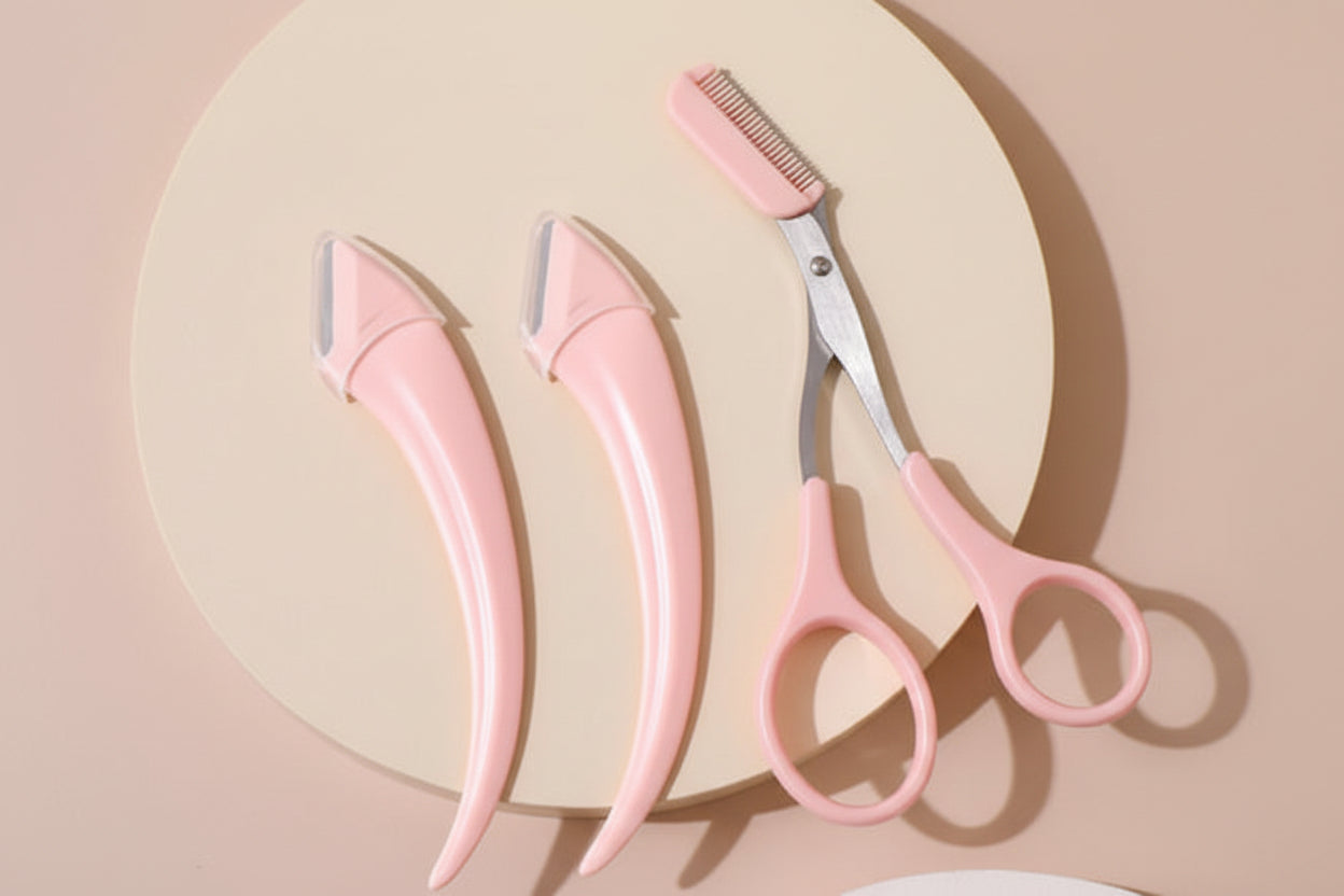 Set of pink grooming tools including a comb, two razors, and scissors on a beige background