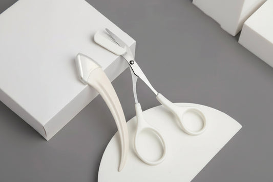 White scissors and hairbrush on a gray surface with a white box.