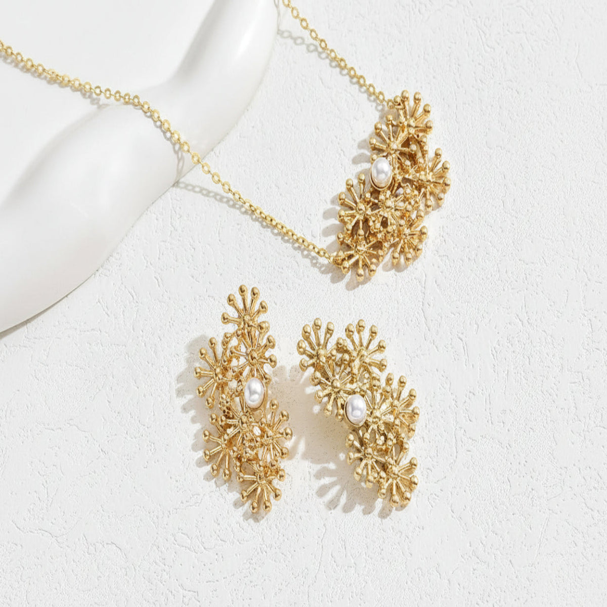 Gold necklace and earrings with pearl accents on a white background