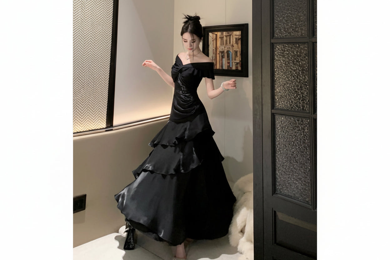 Woman in a black off-shoulder dress standing in a room with a textured wall and framed picture.