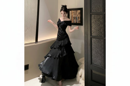 Woman in a black off-shoulder dress standing in a room with a textured wall and framed picture.