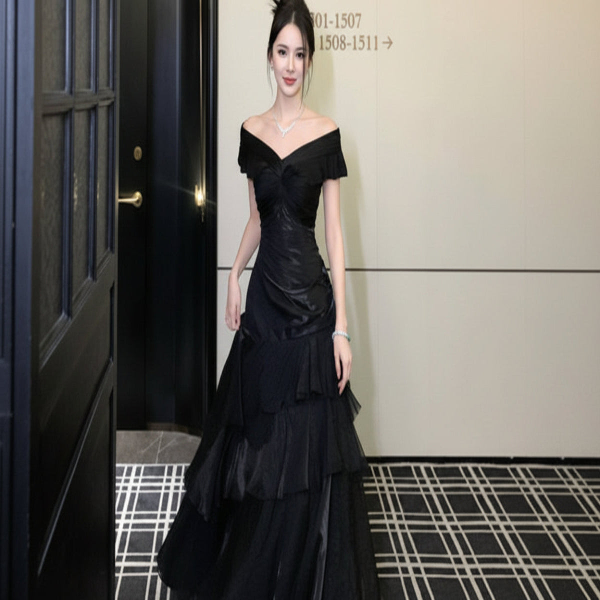 Woman in a black off-shoulder evening gown standing in front of a door.