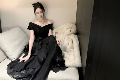 Woman in a black off-shoulder dress sitting on a white couch with a fur throw.