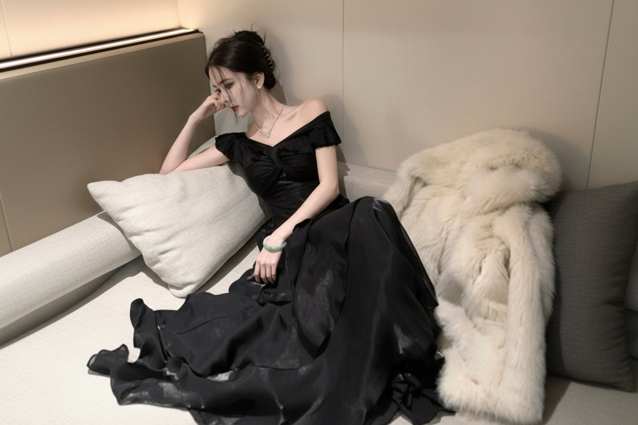 Woman in a black off-shoulder dress sitting on a couch with white fur.