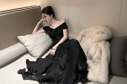 Woman in a black off-shoulder dress sitting on a couch with white fur.