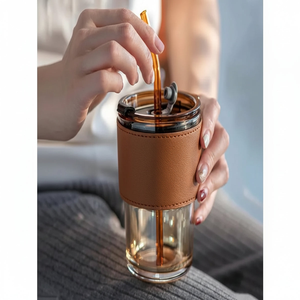 Person using a glass tumbler with a brown leather sleeve and straw.