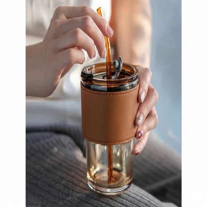 Person using a glass tumbler with a brown leather sleeve and straw.