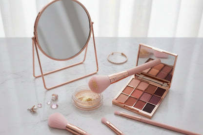Makeup brushes, compact mirror, and eyeshadow palette on a marble surface.