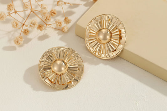 Gold earrings with sunburst design on a light background
