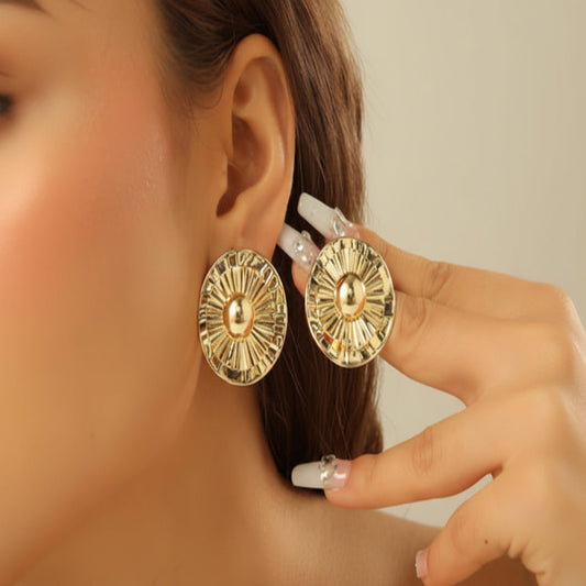 Gold earrings being worn and held up to an ear against a neutral background