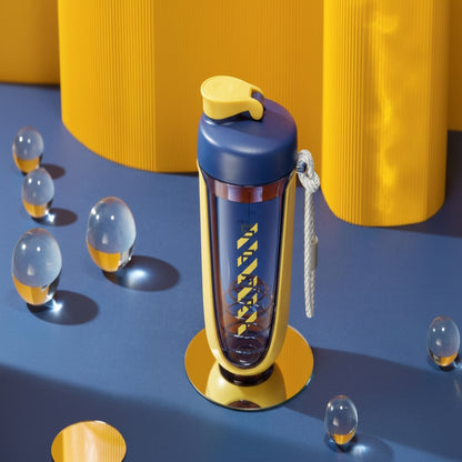 Blue and yellow water bottle with a keychain on a blue surface with yellow cylindrical objects in the background.