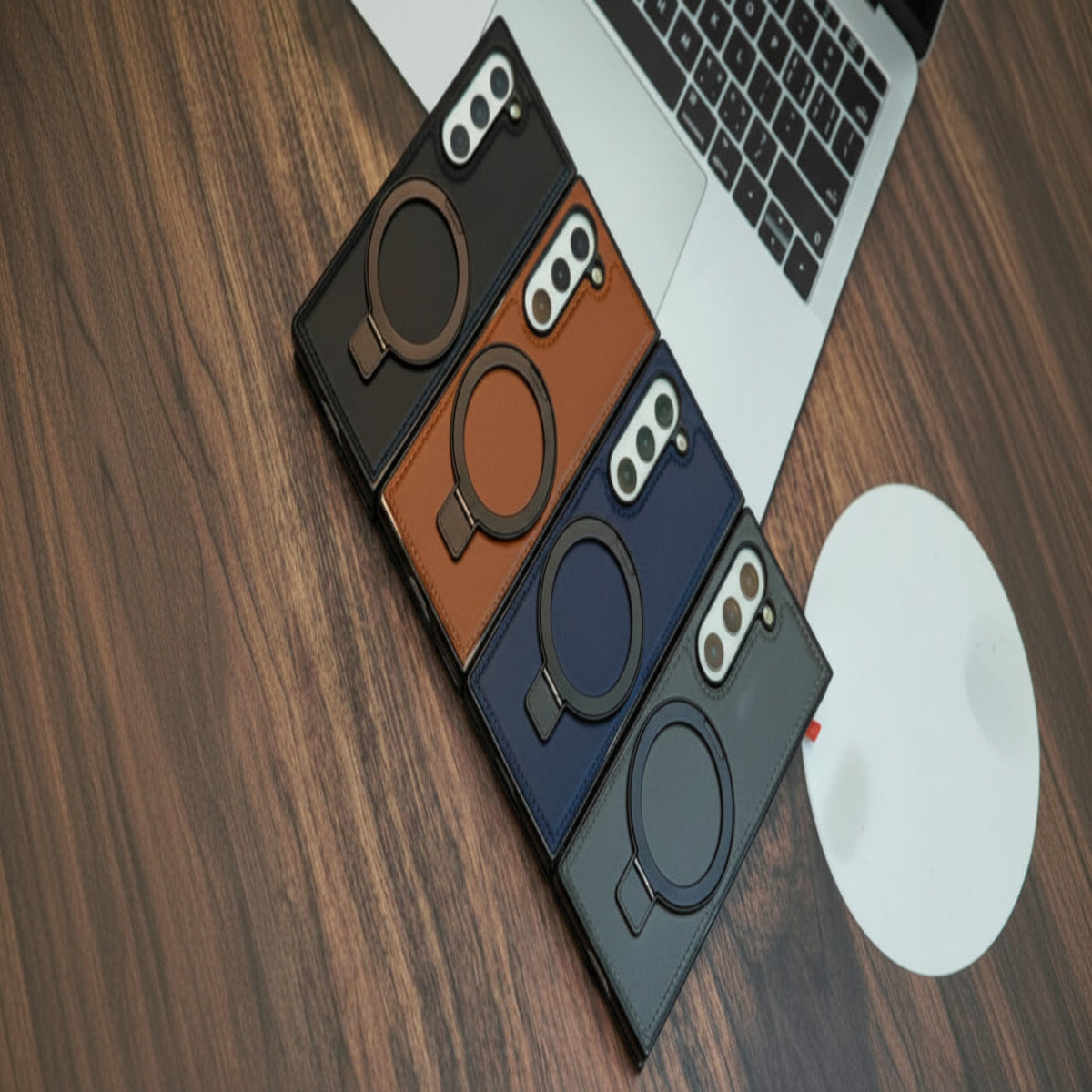 Four phone cases in black, brown, blue, and gray on a wooden surface with a laptop.