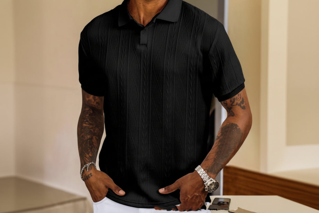 Person wearing a black textured polo shirt with tattoos on arms.