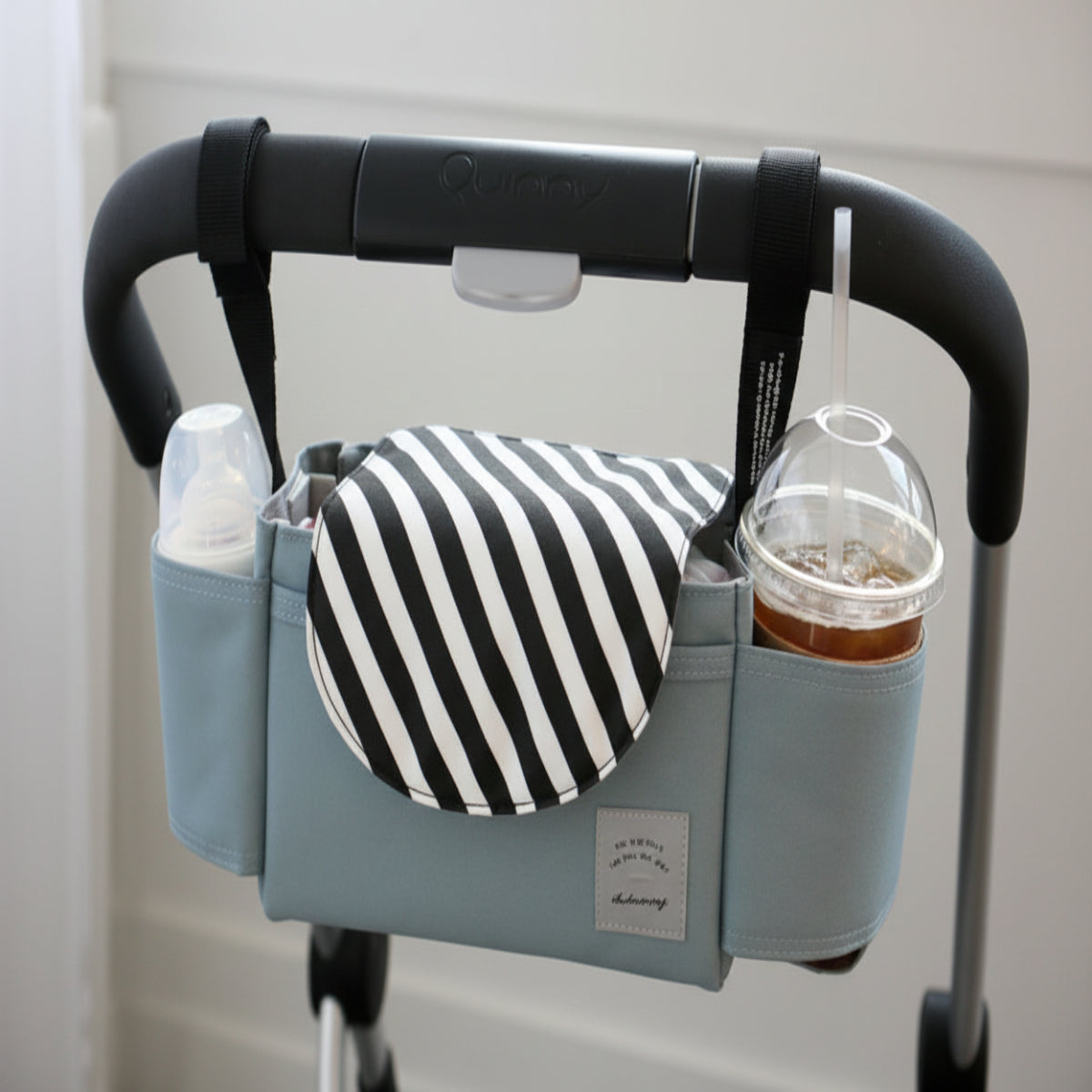 Stroller organizer with cup holder and striped pouch attached to a stroller handle.