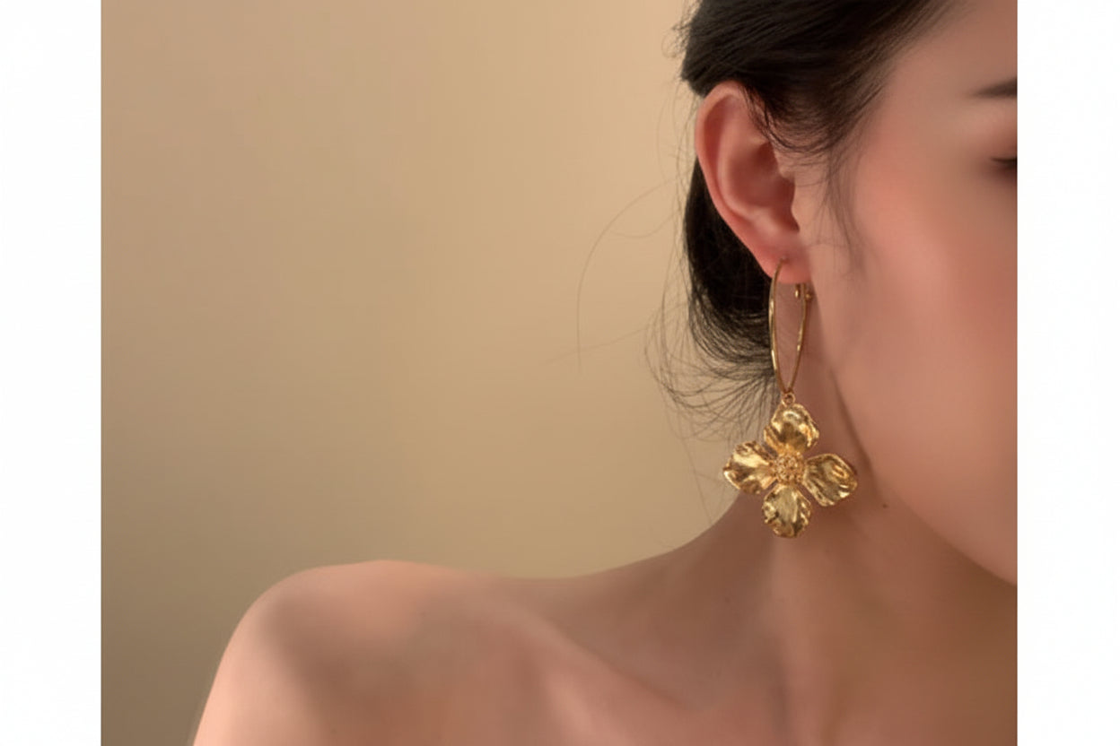 Gold floral earring worn by a person against a beige background