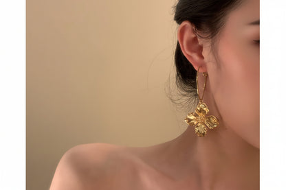 Gold floral earring worn by a person against a beige background