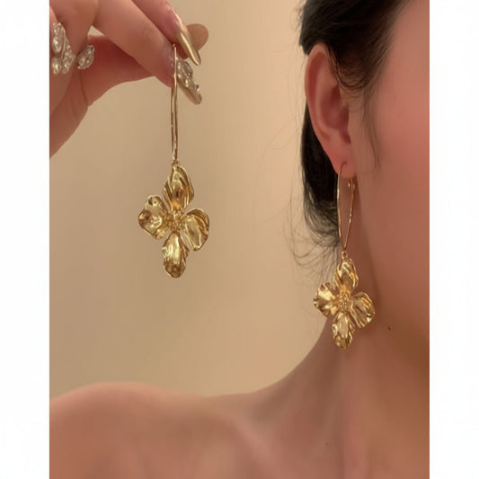 Gold floral earrings being worn by a person against a beige background