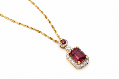 Gold necklace with a red gemstone pendant on a white background