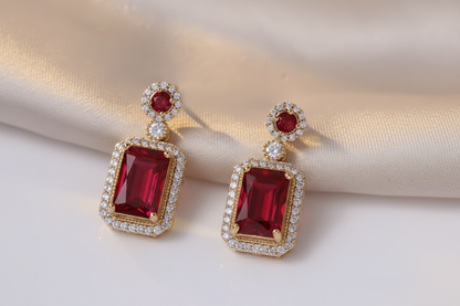 Gold earrings with red gemstones on a light background