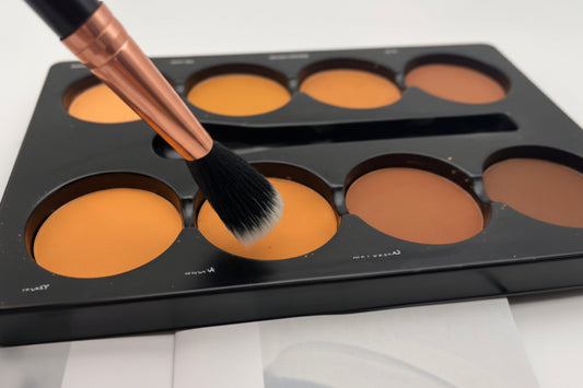 Makeup palette with orange and brown shades and a brush on a white background