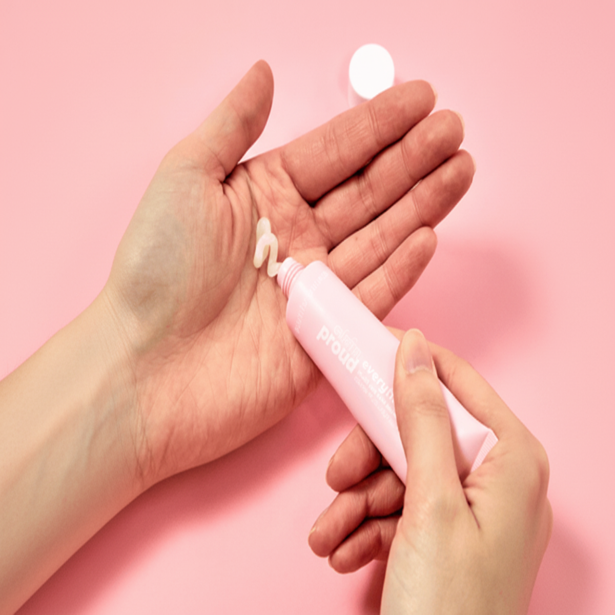Person applying a small amount of pink cream to their palm on a pink background