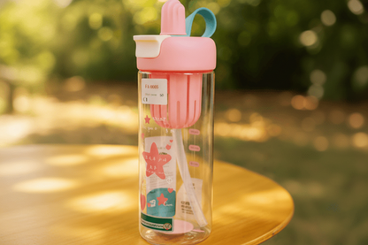 Pink water bottle with a straw and handle on a blurred natural background