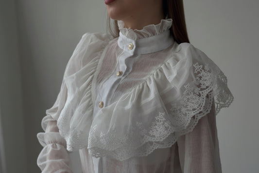 Close-up of a person wearing a white lace blouse with a blurred background