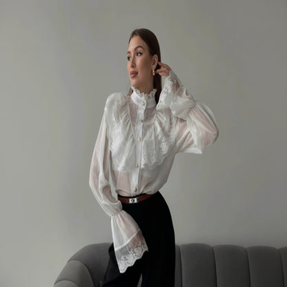 Woman wearing a white lace blouse and black pants sitting on a gray couch.