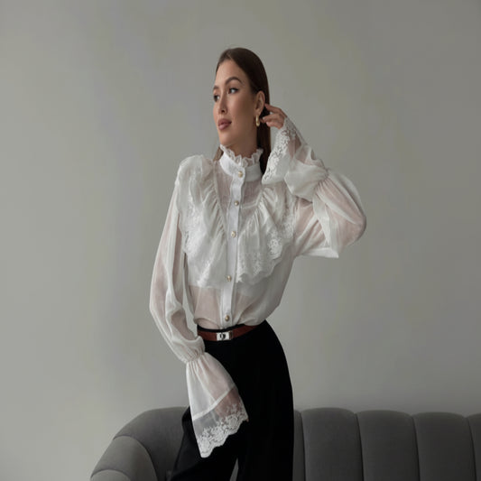 Woman wearing a white lace blouse and black pants sitting on a gray couch.