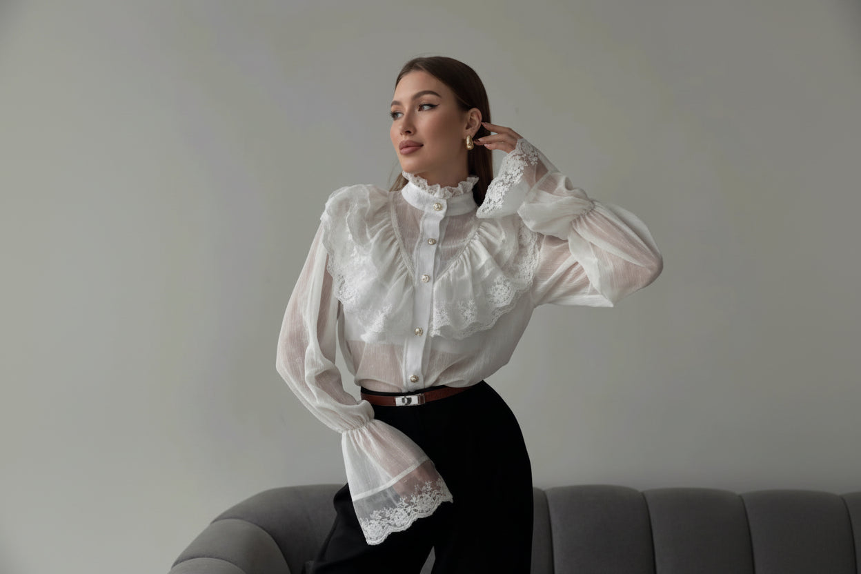Woman wearing a white lace blouse and black pants sitting on a gray couch.
