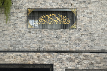 Decorative wall art with gold Arabic calligraphy on a stone wall.
