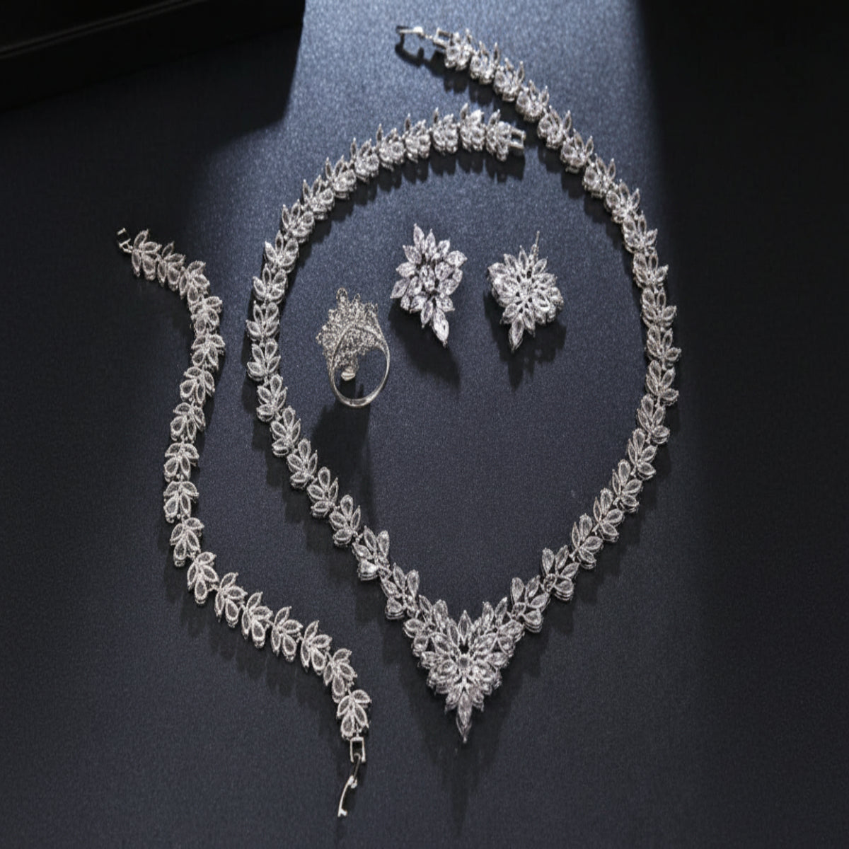 Silver jewelry set including necklace, bracelet, ring, and earrings on a dark surface
