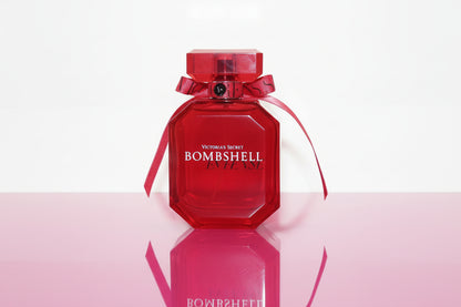Red 'Bombshell' perfume bottle with a ribbon on a wooden surface