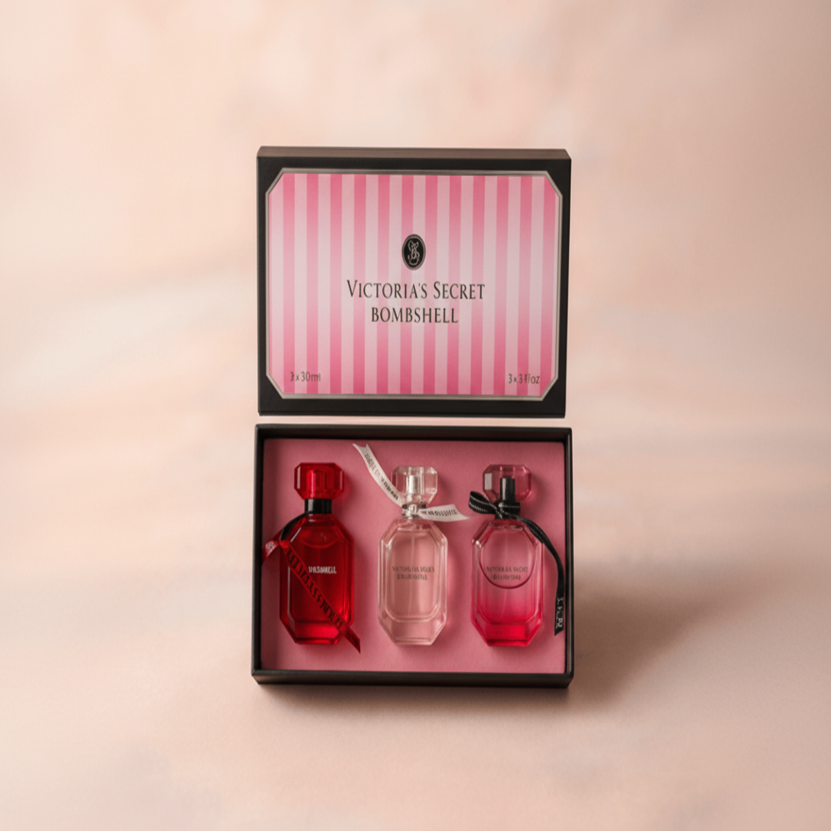 Victoria's Secret Bombshell perfume set with three bottles in a decorative box on a pink background.