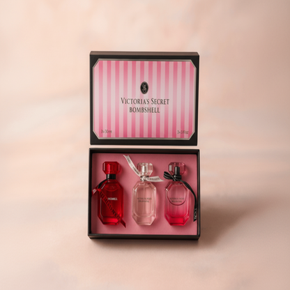 Victoria's Secret Bombshell perfume set with three bottles in a decorative box on a pink background.