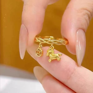 Gold ring with a unicorn charm held between fingers against an orange background