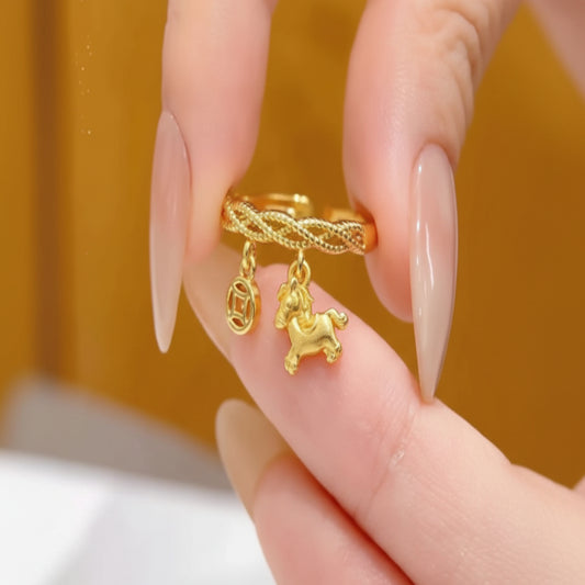 Gold ring with a unicorn charm held between fingers against an orange background