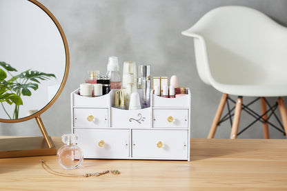White cosmetic organizer with various items on a wooden surface, with a mirror and plant in the background.